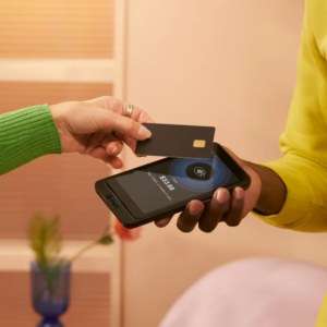 image of green jumper-wearing person tapping a card agaisnt a phone held my a person in a yellow jumper